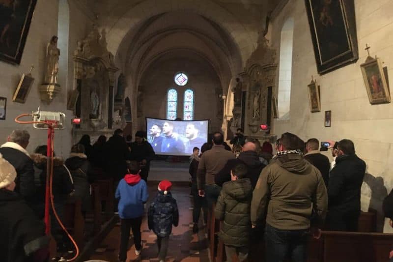 Toutes les générations sont rassemblées dans l'église de Courcelles pour voir la finale France -Argentine ;deux enfants avec leur bonnet rouge déambulent dans la nef
