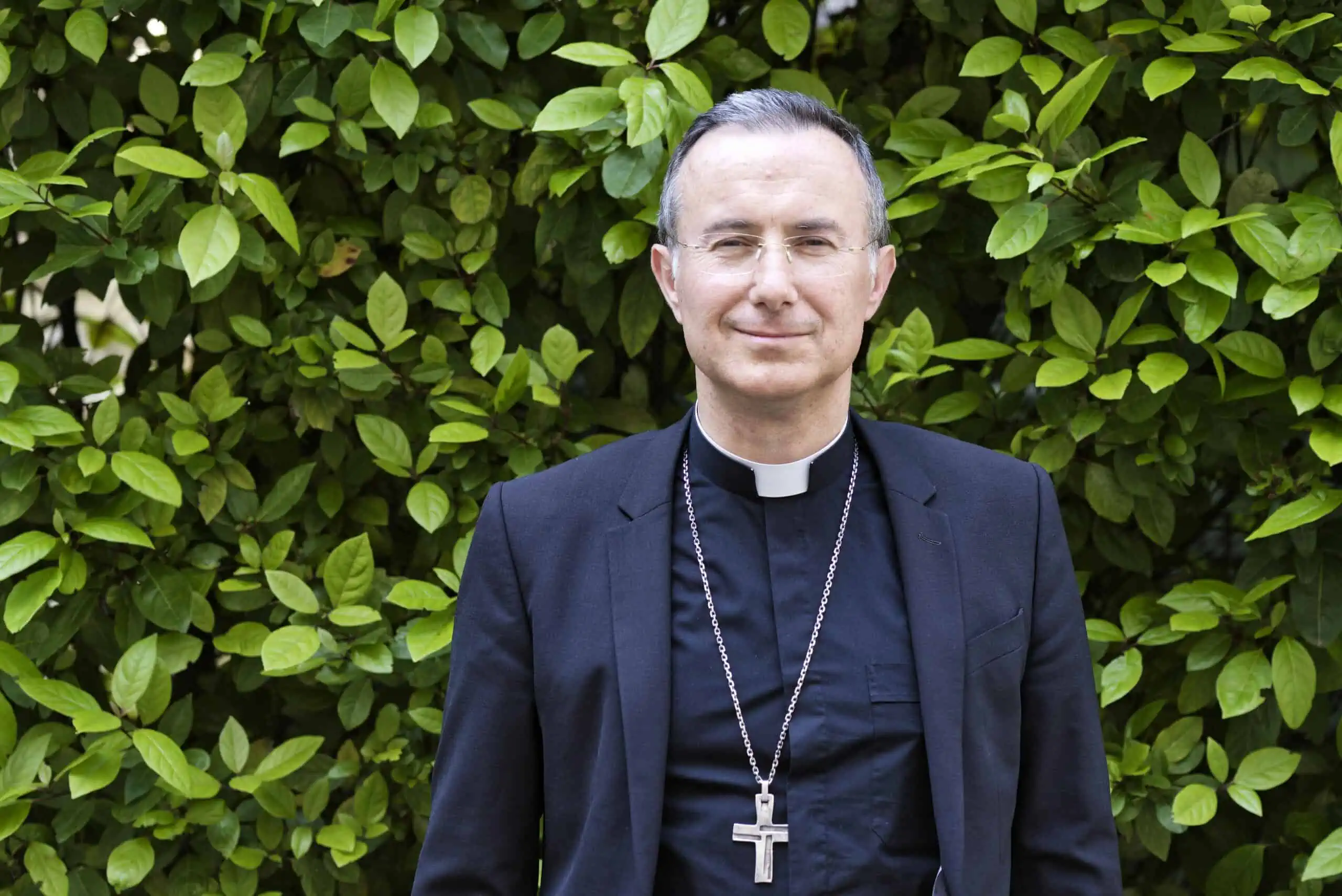 Mgr Jean-Pierre Vuillemin en clergyman devant une haie de plantes vertes