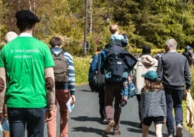 De dos des pélerins qui marchent avec un petit enfant sur les épaules d'une adulte, un jeune marcheur a un béret basque et un tee-shirt vert