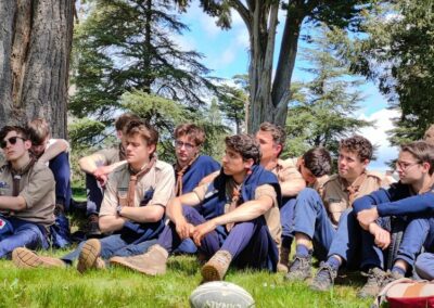 Dans une prairie une dizaine de jeunes scouts écoutent un témoignage